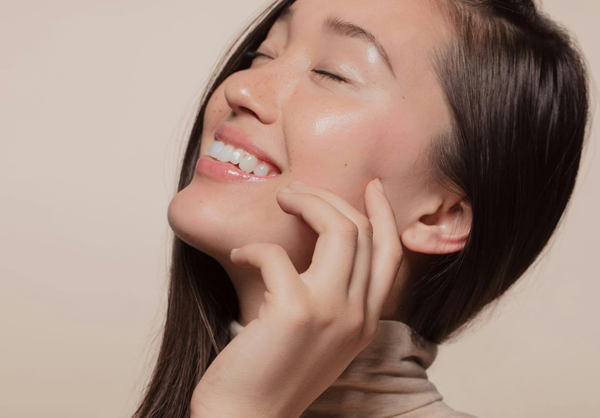 Smiling dark haired woman touching her face.
