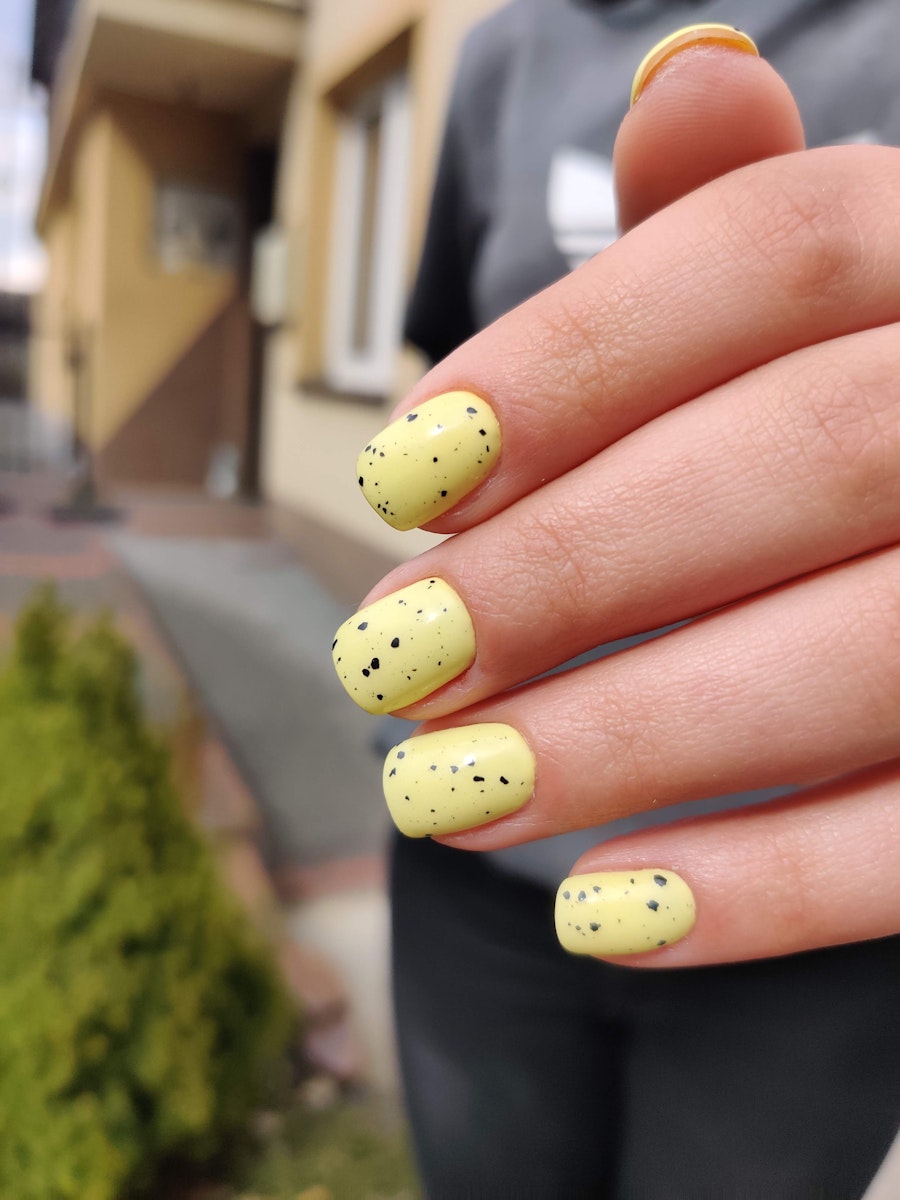 Pastel yellow splatter design on square nails with round corners