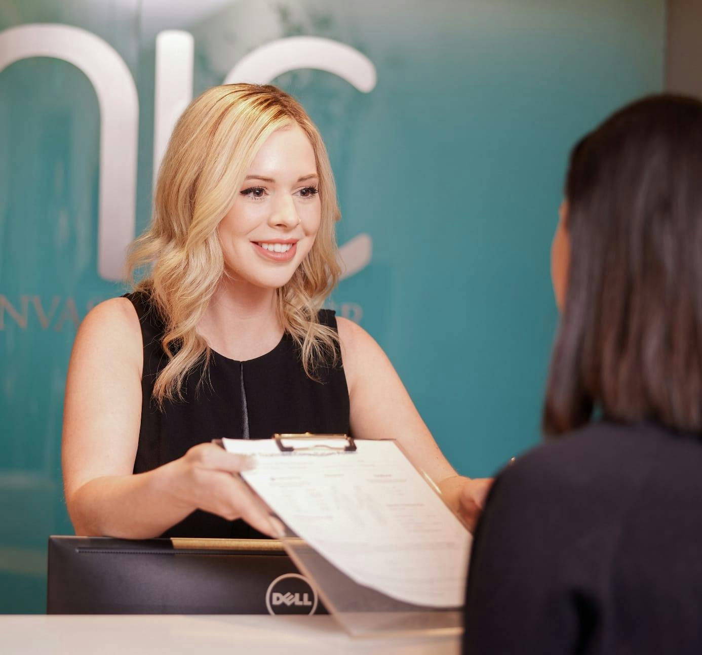 Smiling Enic Receptionist Handing over patient forms