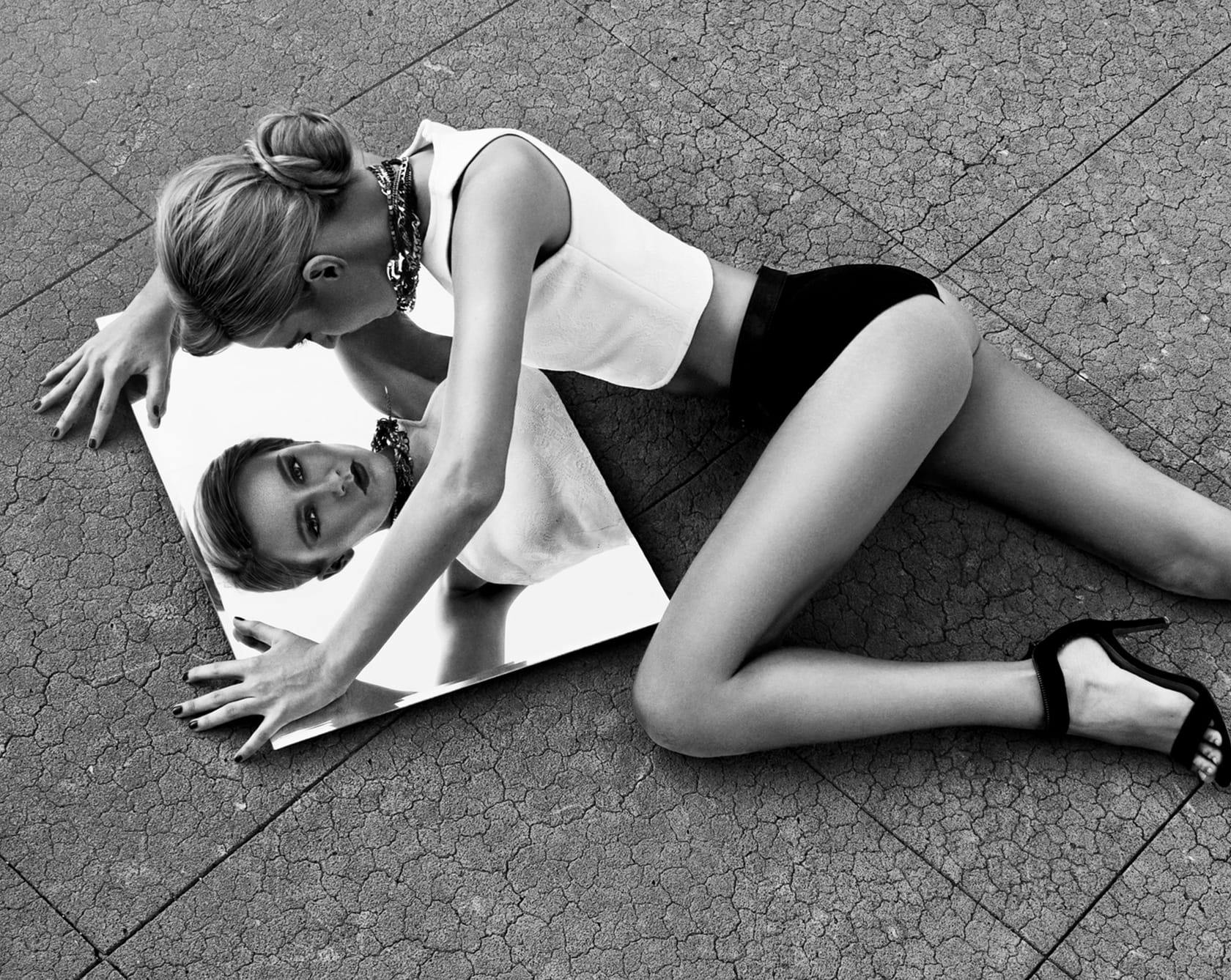 a black and white image of a woman laying on the ground above a mirror looking down at their reflection