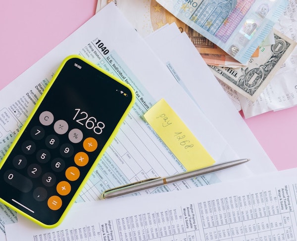 A pile of money and paperwork, with a pen and calculator.