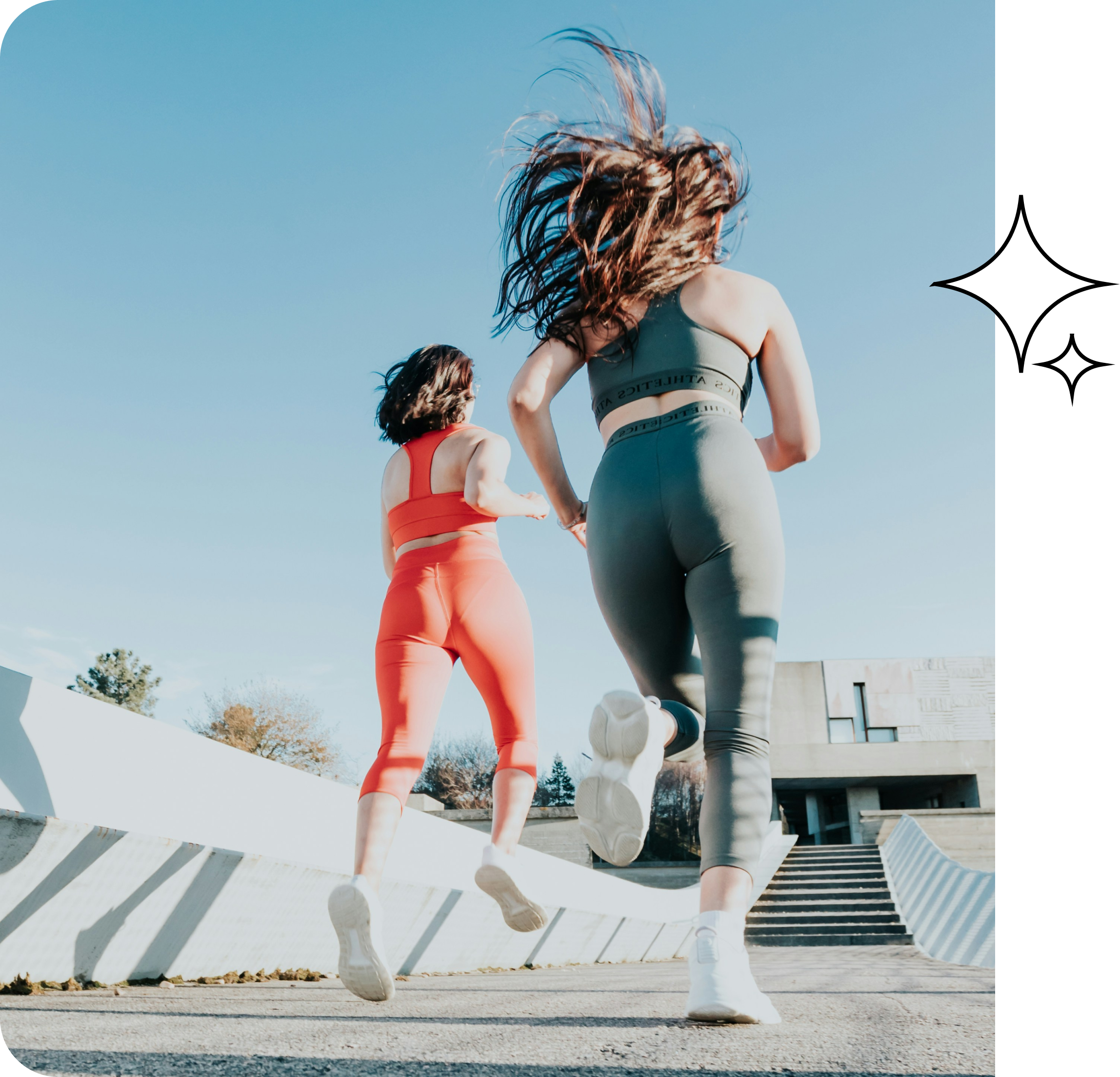 Two women in colorful athletic wear run outdoors on a sunny day, with modern buildings and blue sky in the background. Their hair flows behind them as they move up concrete steps. A sparkle graphic decorates the right corner.
