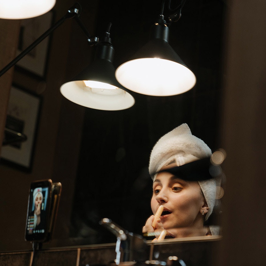Woman in front of mirror applying lipstick