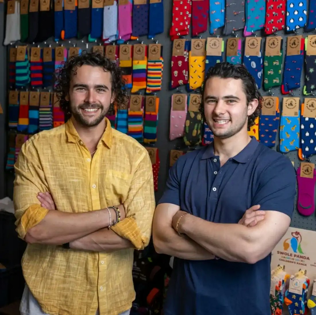 Oliver and James Slacke, founders of Swole Panda, in front of a wall of socks