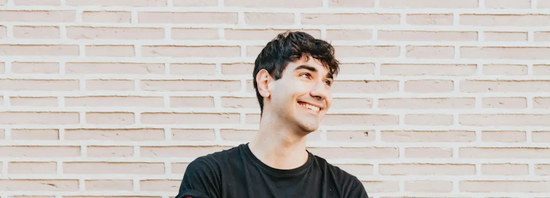 Smiling person with black t-shirt standing in front of a light brick wall