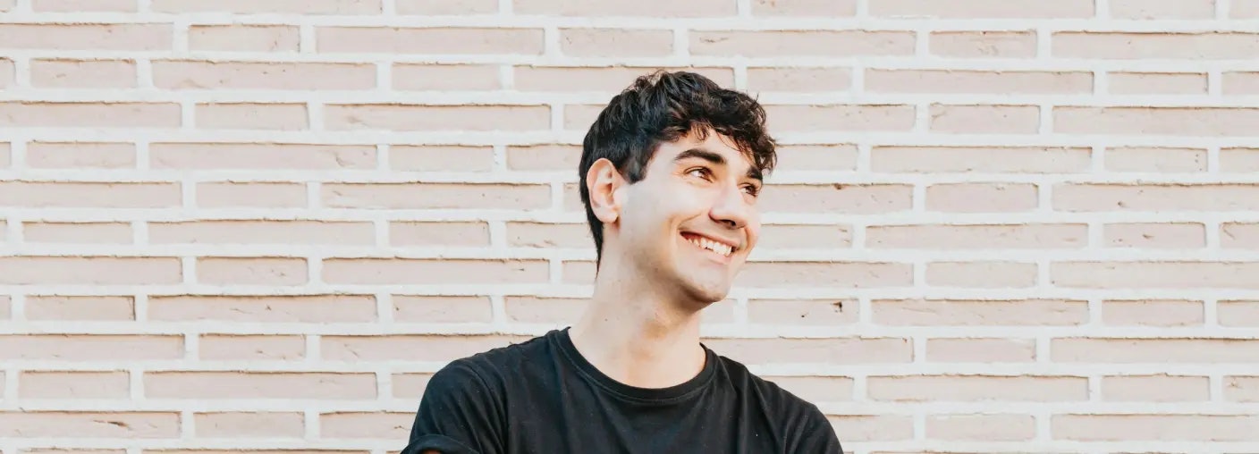 Smiling person with black t-shirt standing in front of a light brick wall