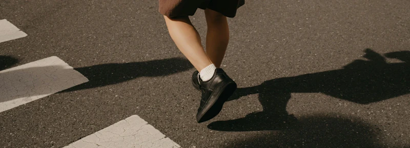 Person walking across the street, shot from ground level focusing on feet and ankles.