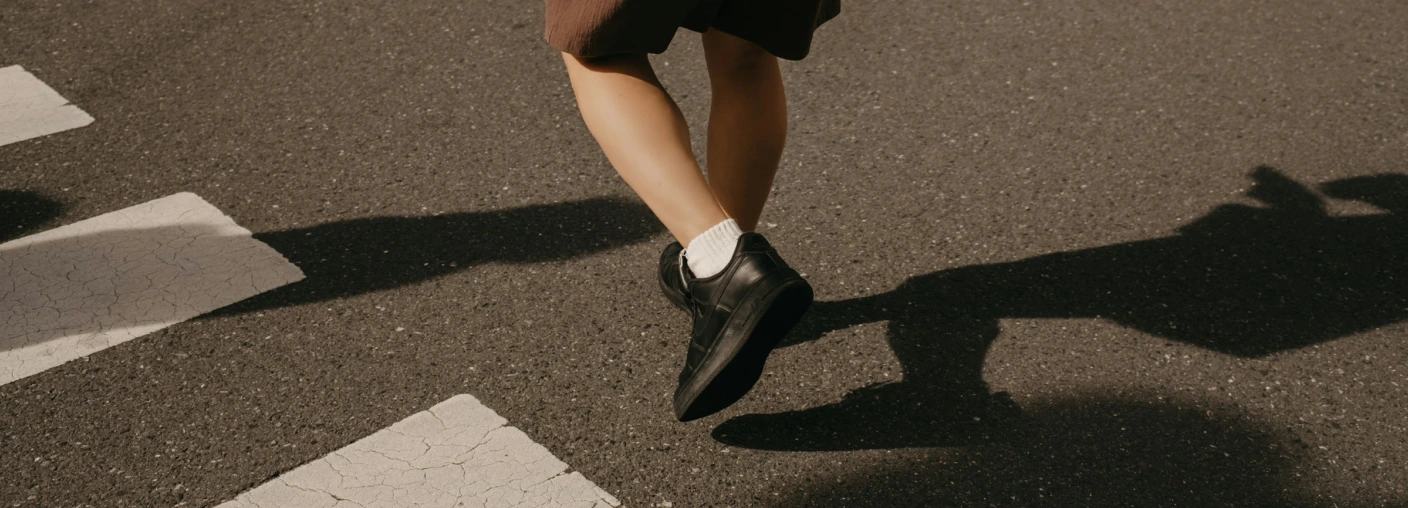 Person walking across the street, shot from ground level focusing on feet and ankles.