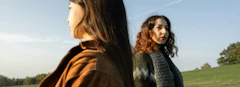 two women looking in opposite directions, standing on grass field, considering their options