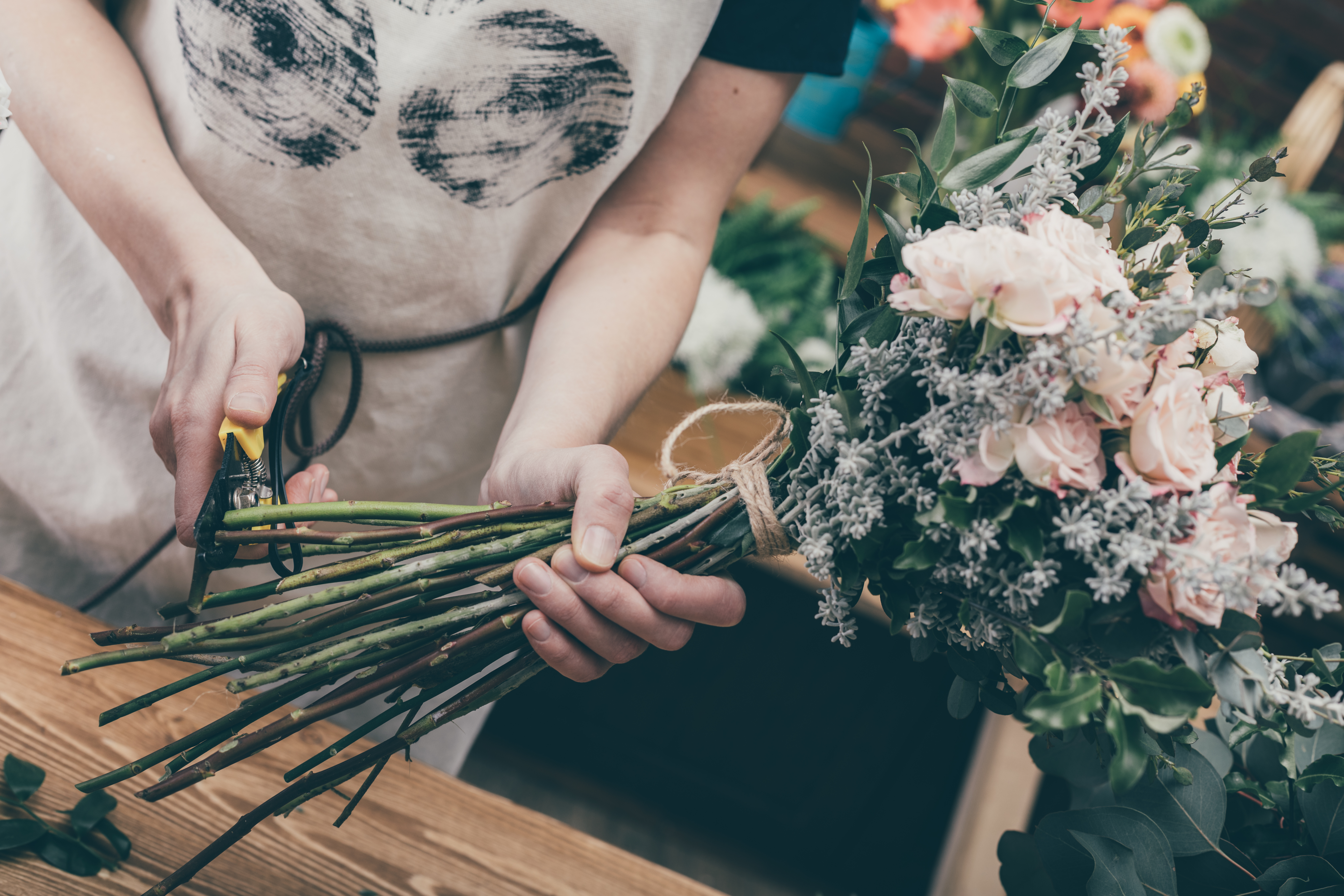 A florist holding a bunch of flowers and trimming the bottom of the stems