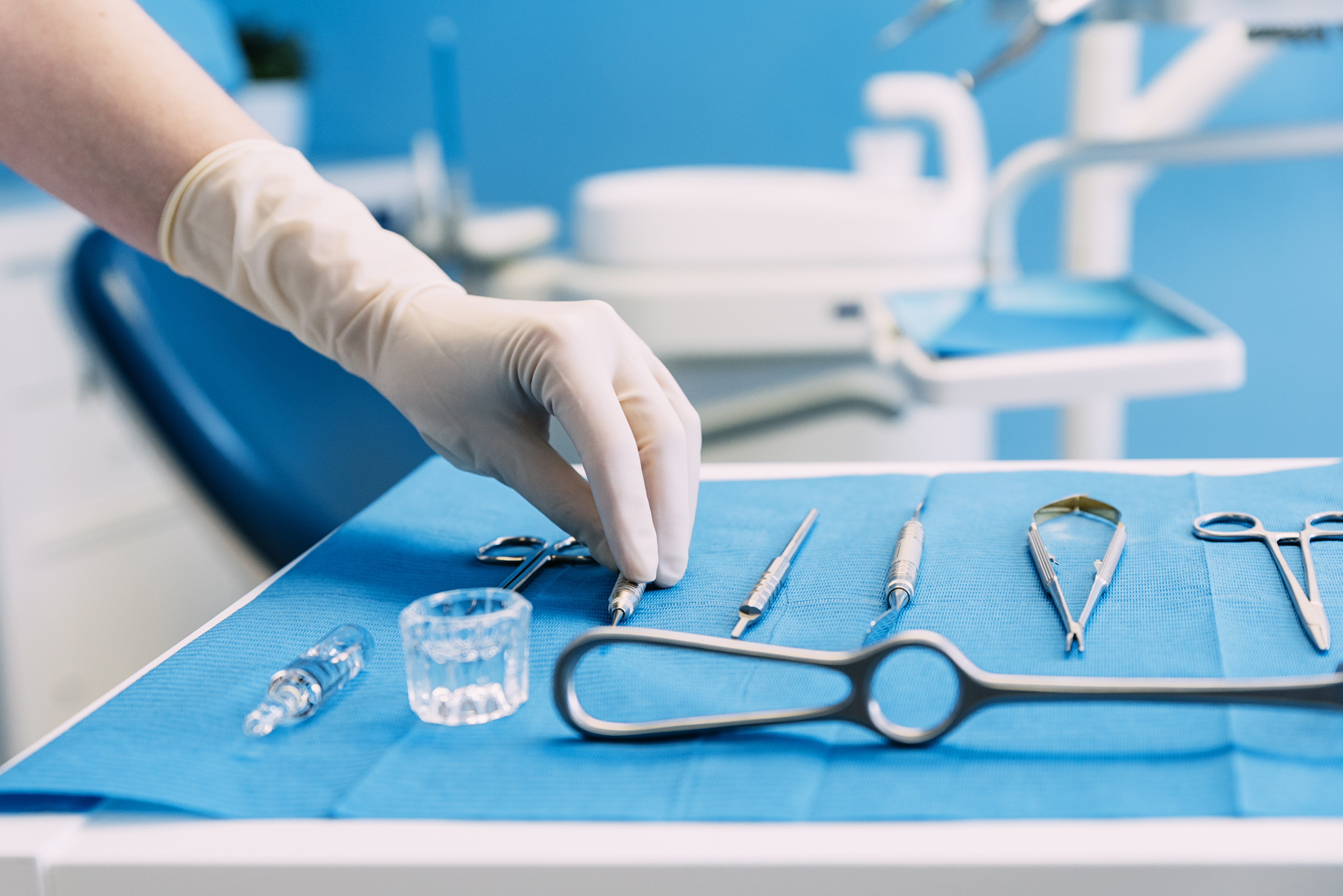 Gloved hand picking up a dental tool from a selection of dental equipment