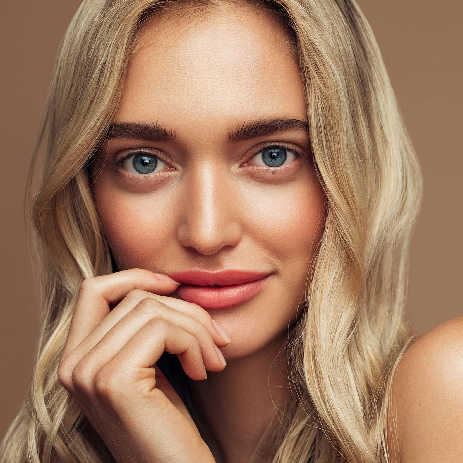 Woman with blonde hair smirking, hand near her mouth