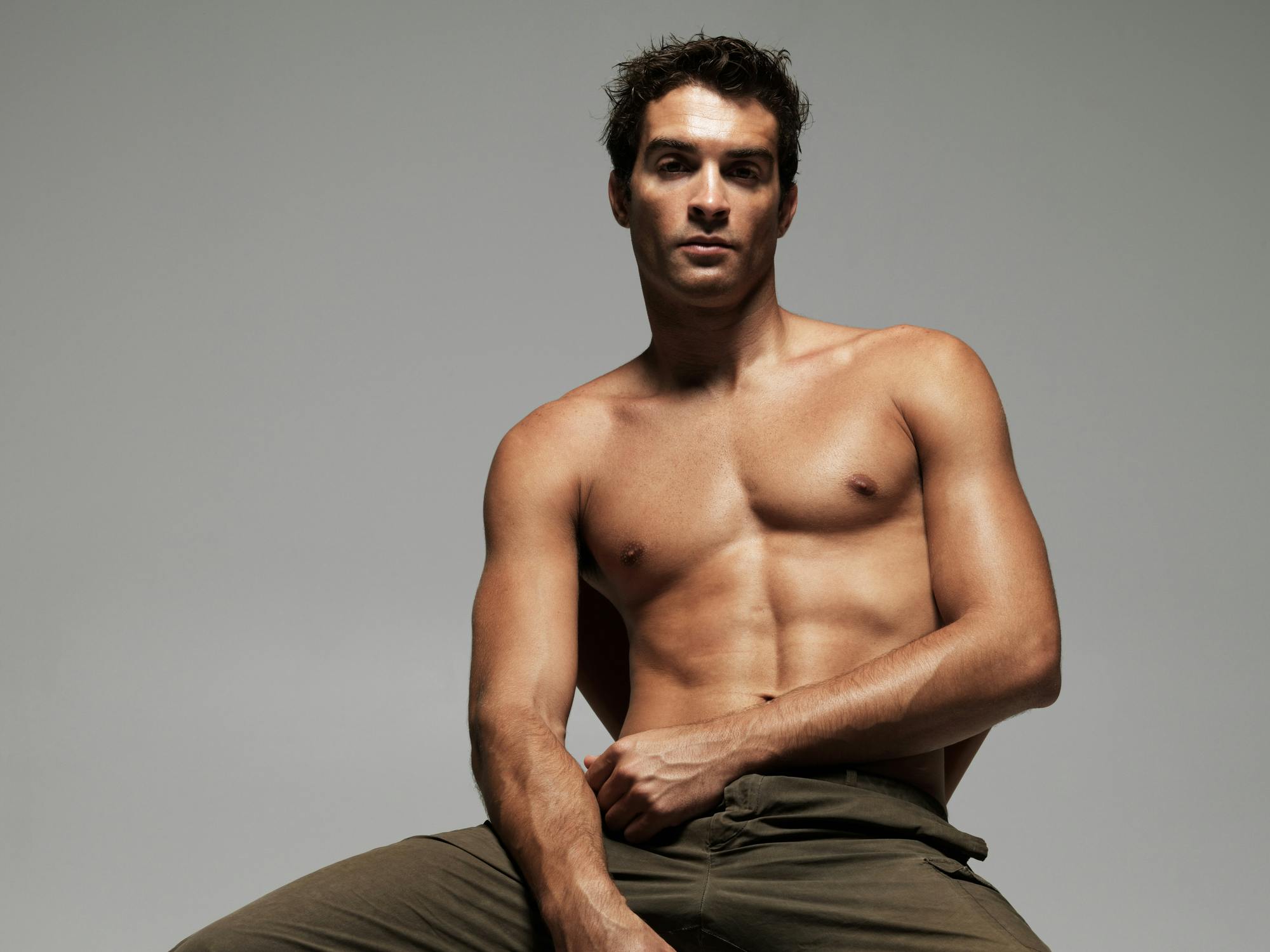 Muscular shirtless man sits in a chair in a studio shoot. His hairless chest shows off the possible results of having laser hair removal in Long Beach with Marcus Medical