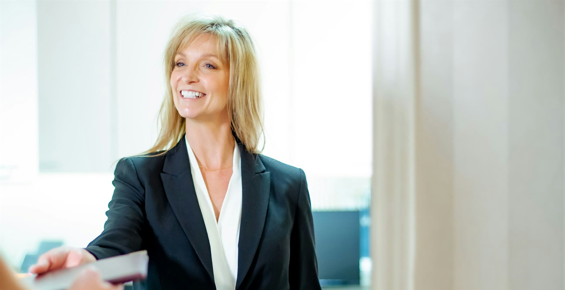 Blonde woman in a suit jacket handing forms to someone