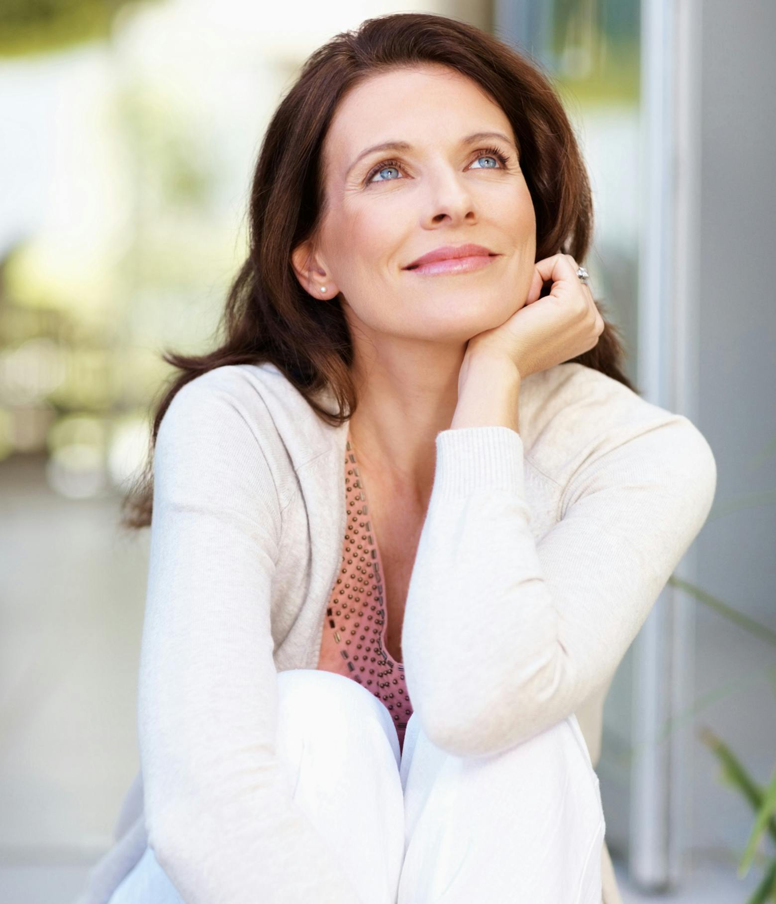 Beautiful middle aged woman sitting, looking up while resting her face on her hand