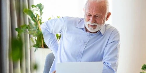 older man with poor posture and back pain in front of computer