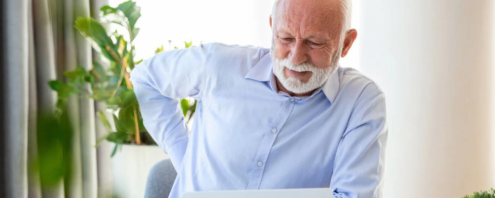 older man with poor posture and back pain in front of computer