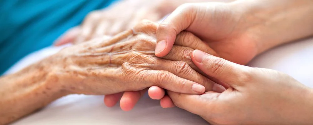 Older person holding loved one's hand in hospice care