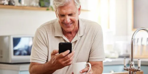 older man with coffee doing research on phone
