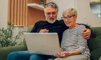 Older couple sitting on couch reading Medicare explained guide on computer