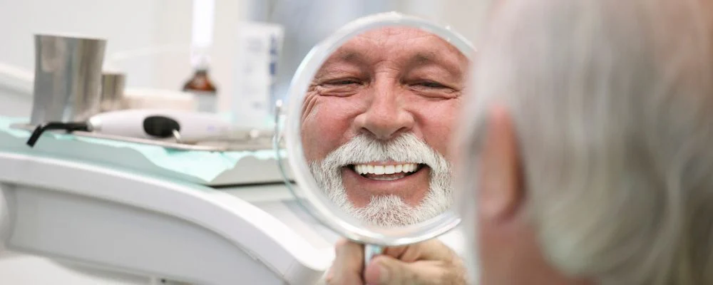 older man looking in mirror smiling at orthodontist office