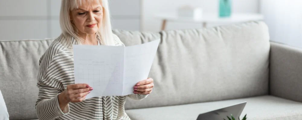 older woman on couch comparing two papers