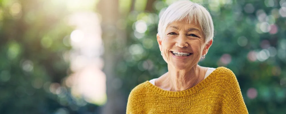 Older woman smiling in front trees