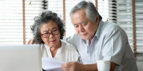 Older couple thinking and looking through papers and computer
