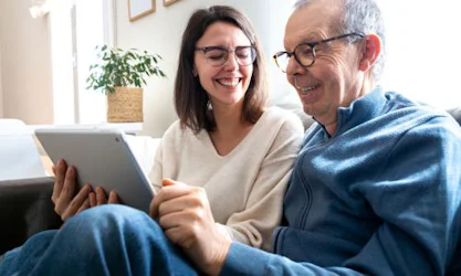 Father and daughter sitting on couch in living room with tablet