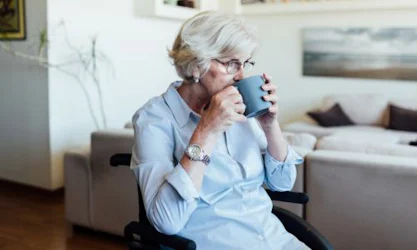 65 year old woman in wheelchair at home sipping from mug