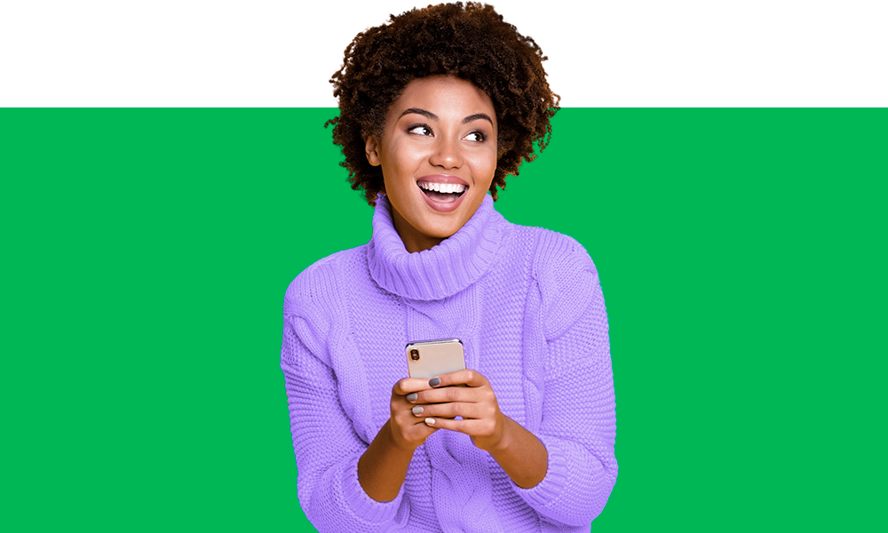 em fundo verde vibrante, mulher sorridente aparece de suéter lilás enquanto segura um celular.