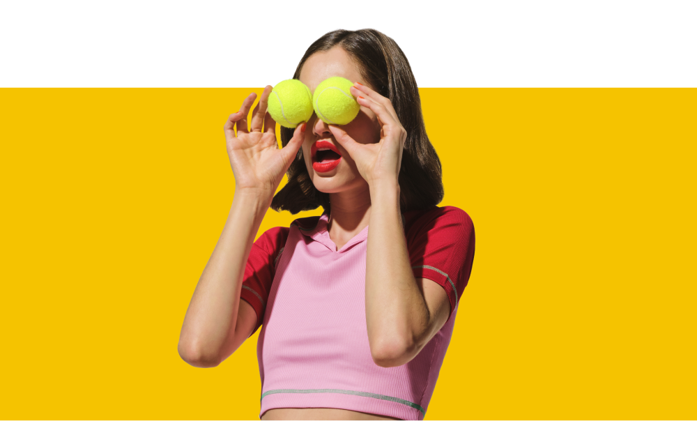 modelo faz pose engraçada enquanto segura duas bolas de tênis, uma com cada mão, cobrindo ambos os olhos.