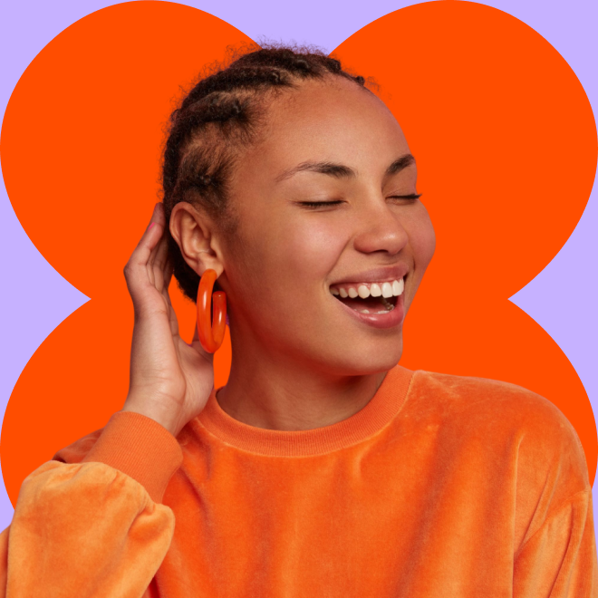 foto de uma modelo sorrindo, do busto pra cima. veste blazer azul, blusa branca, brincos longos, cabelo liso para trás e sombra branca nos olhos.