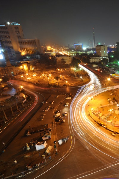 A shot of a large roundabout in the city at dusk as if taken from a tall building—illuminated in gold light by car headlamps