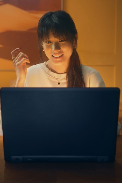 A young woman sits at her childhood bedroom desk in front of her laptop. She is learning how to buy gold for the first time.