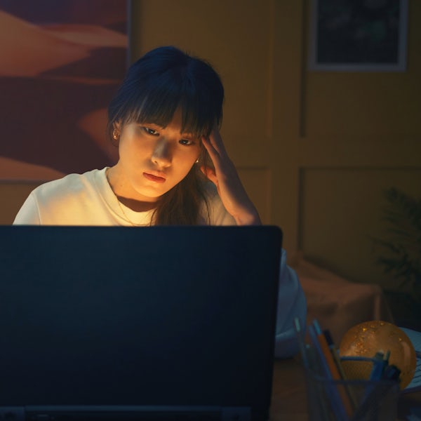 A young woman sitting at a laptop on her desk in her bedroom. She is learning about investing in gold safely.