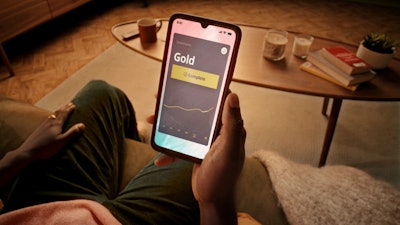 Man sitting on a couch with a large phone in hand buying gold online