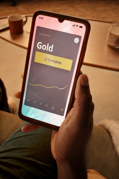 Man sitting on a couch with a large phone in hand buying gold online