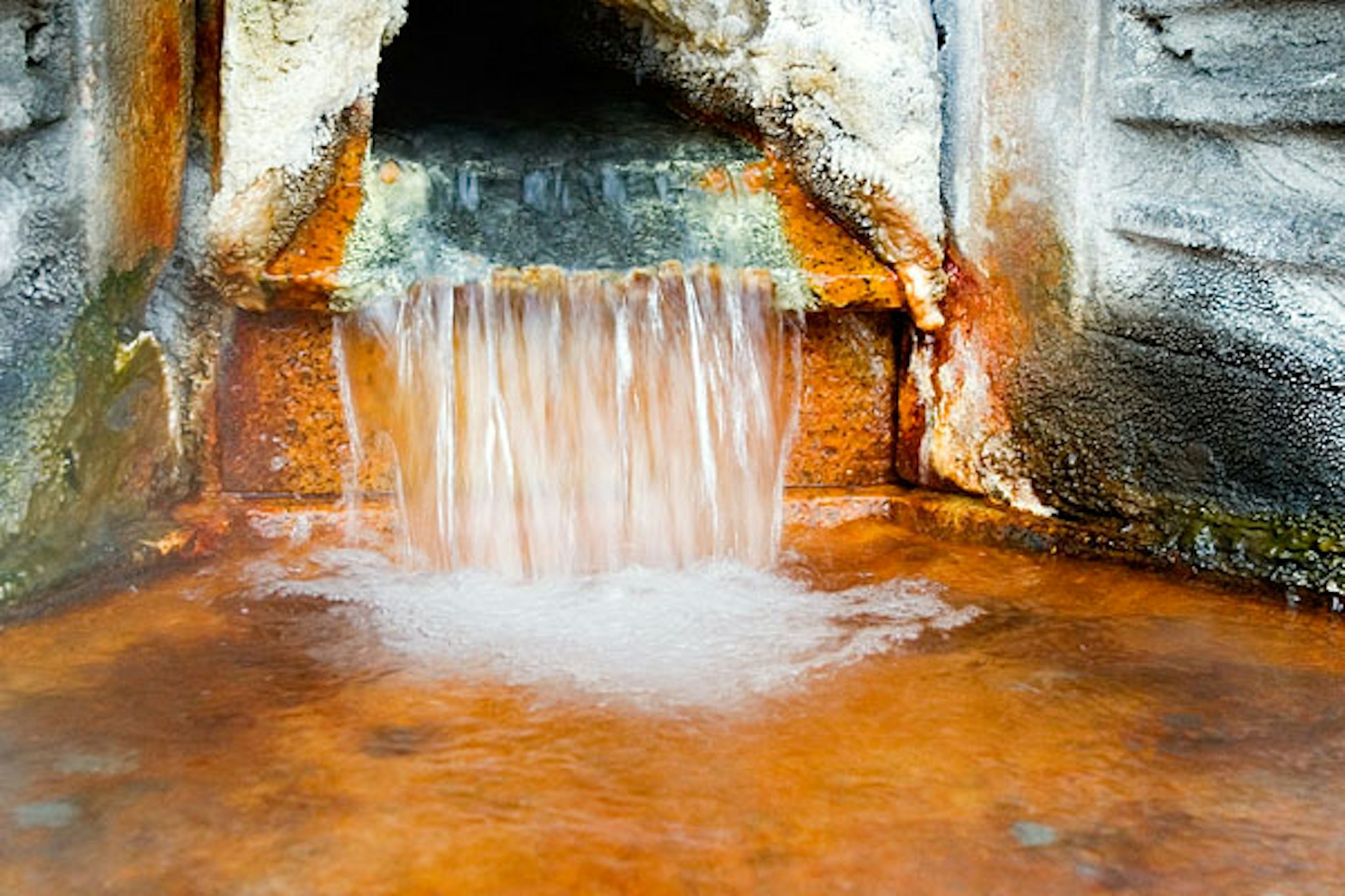 A rusty drainage pipe with water pouring out onto the ground.