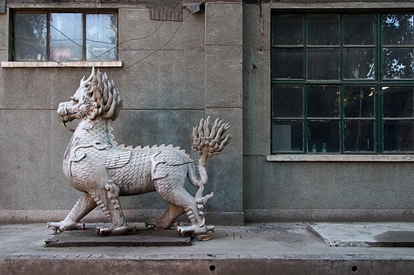 Dragon statue outside building with graffiti and barred windows.