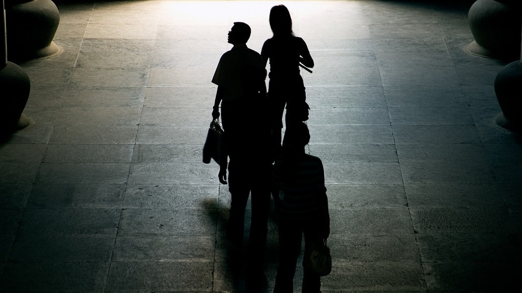 Un gruppo di persone stanti vicino a loro, sul cancello scuro durante la notte con una sorgente luminosa alle loro spalle.