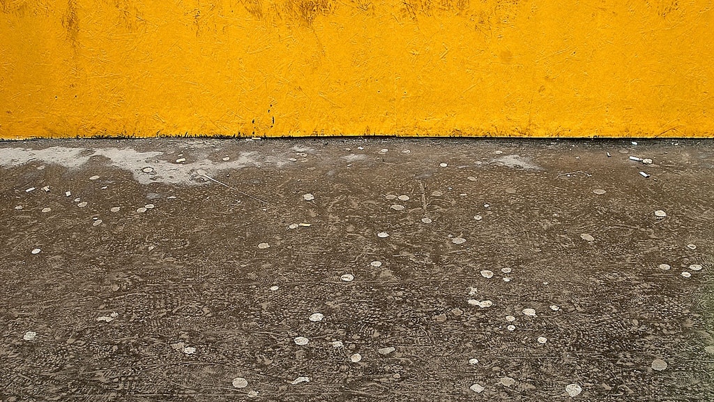 A yellow wall, a patch of dirt ground, a grey pavement.