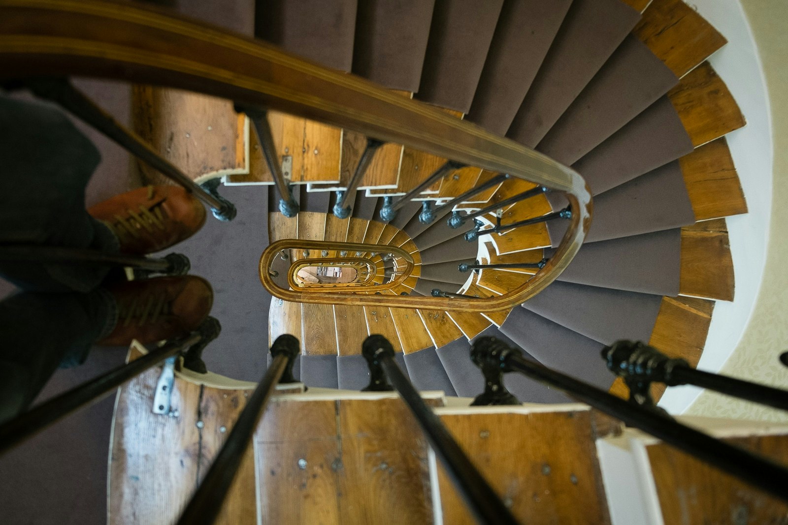 Spiral staircase with wooden bannister and metal railings, viewed from below.