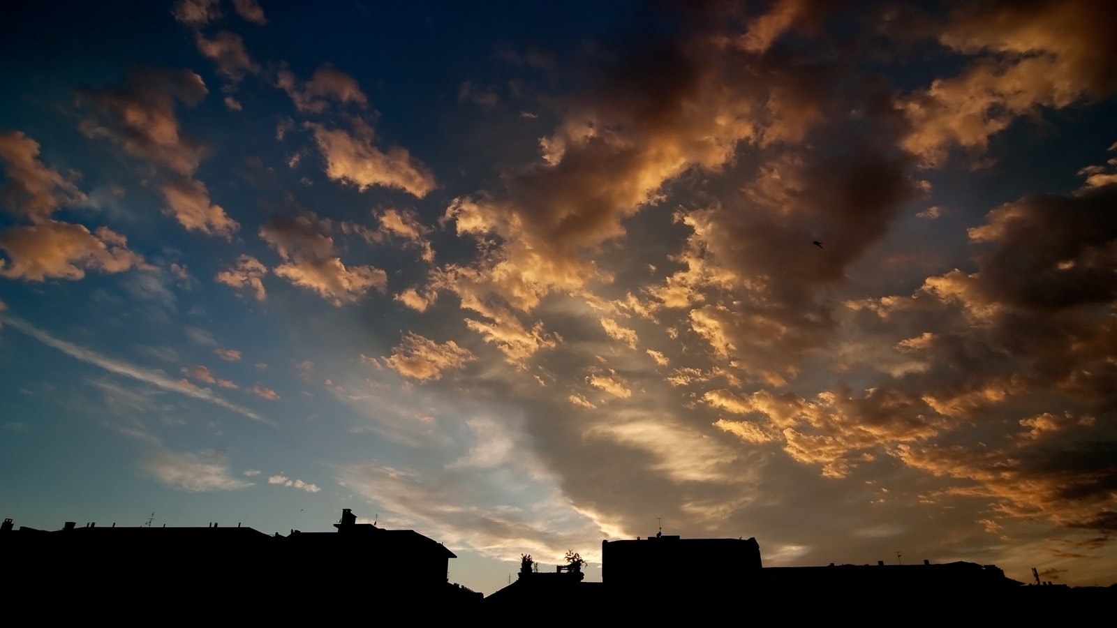Cloudy sunset sky with silhouettes of buildings in the foreground.