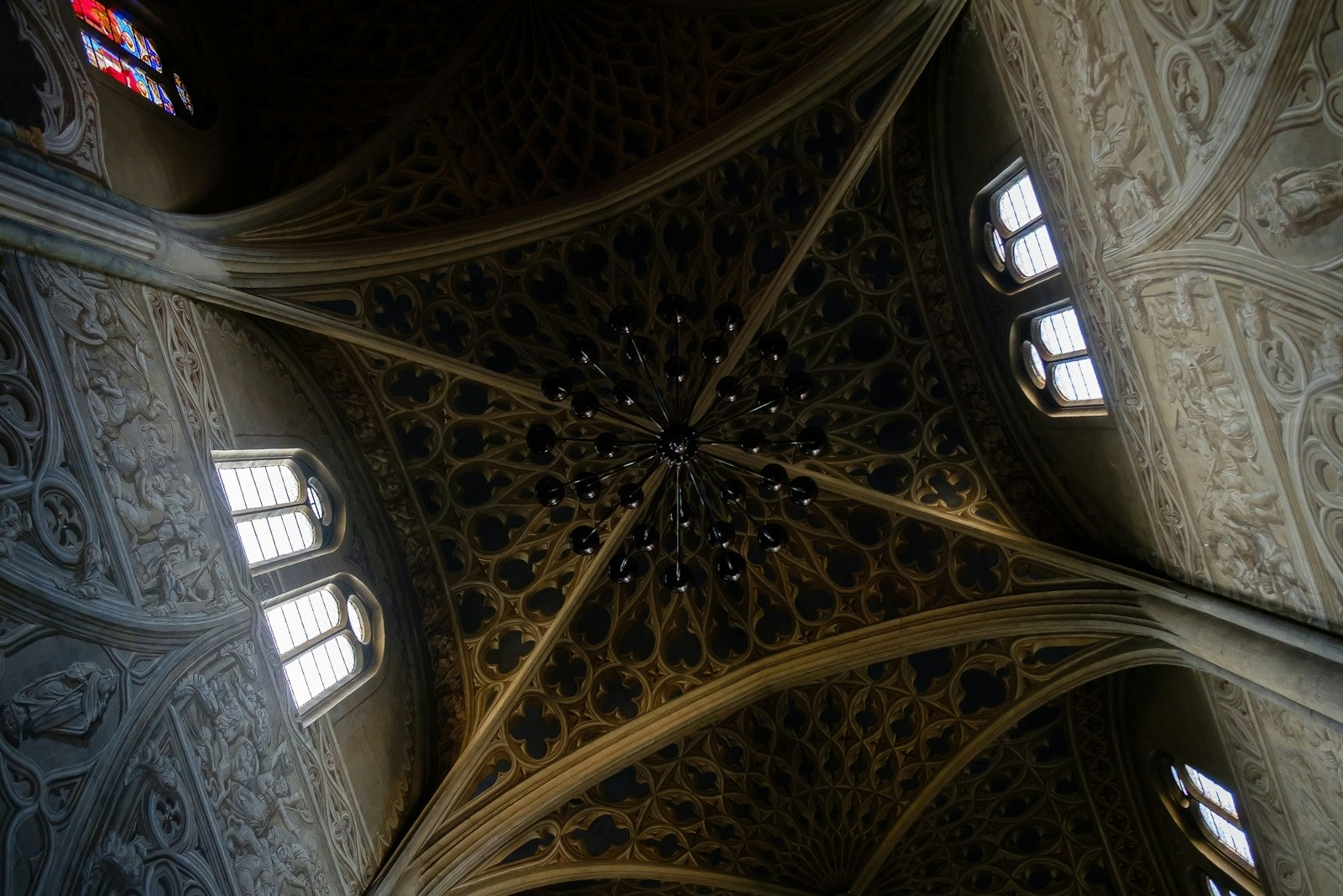Vaulted arches on the ceiling of a cathedral with stained glass windows.