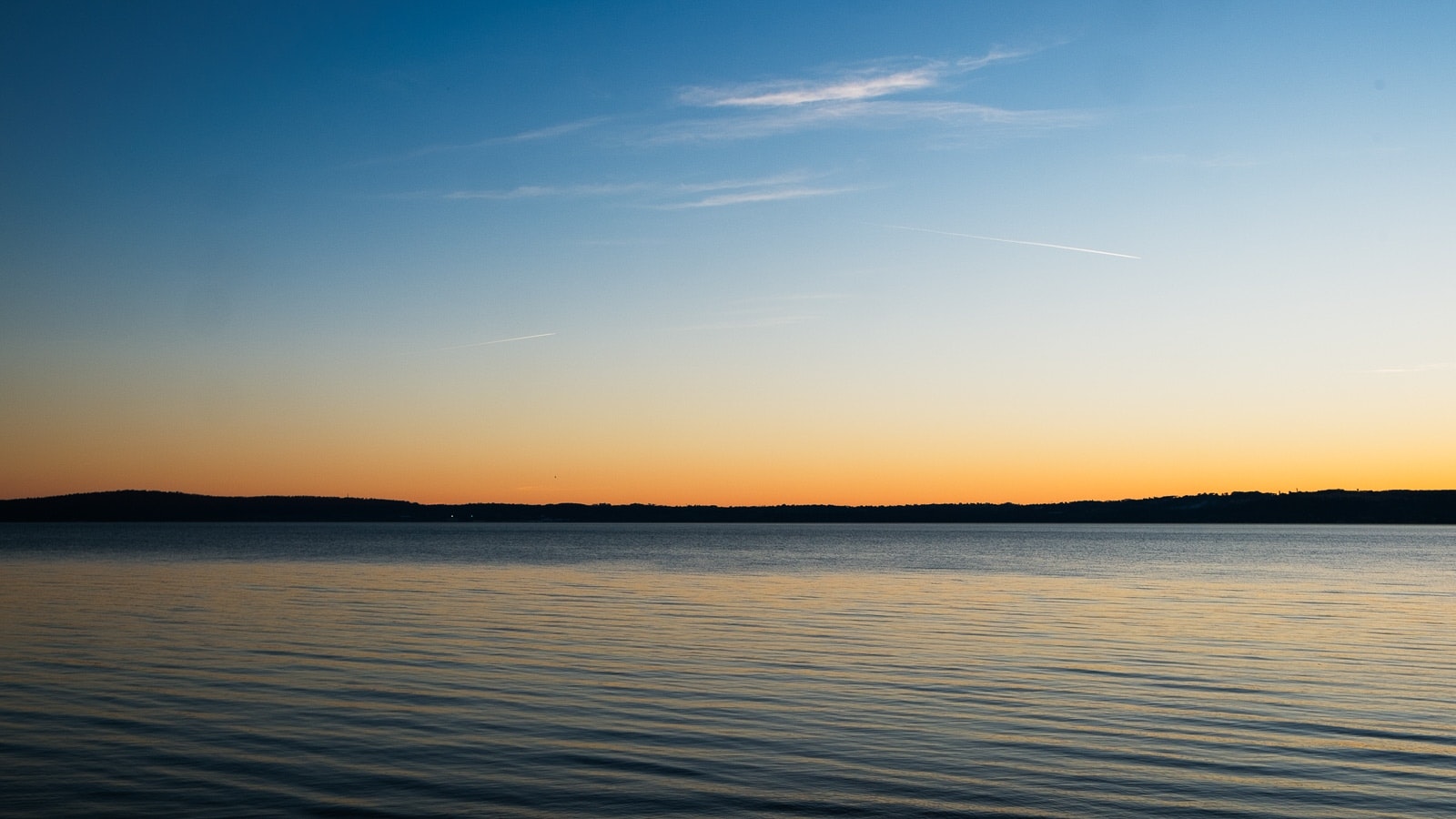 Paesaggio panoramico del tramonto che offre una vista tranquilla su un corpo d'acqua calmo con isole, profilo di una città, silhouetta dei pini e gradiente dolce dall'indomani alla notte.
