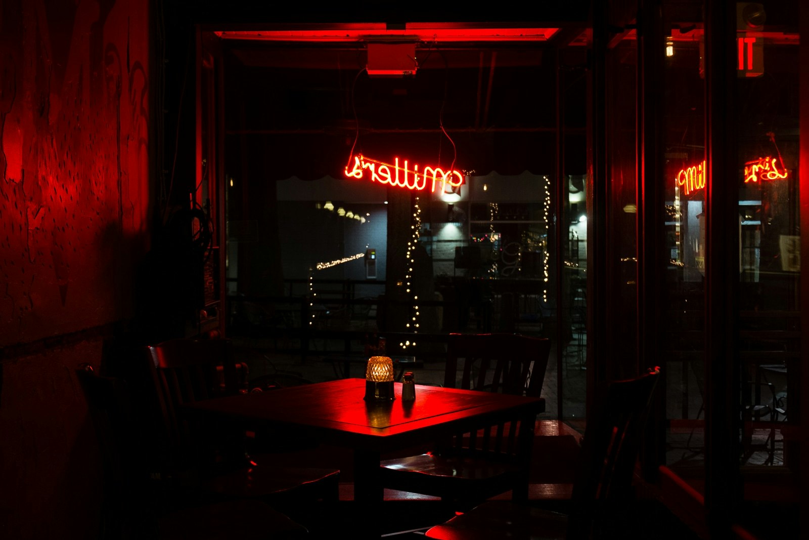 La scena mostra un ambiente di ristorante poco illuminato con lampade rosse che si estendono lungo il corrido. Tavolo vuoto che si trova sotto una finestra, controfine con una vetrata e sessili in primo piano, e un controbanco con sedie lungo la parte avanti. In fondo ci sono delle lampade rosse che brillano accanto a una parola su un supporto. L'atmosfera calda e intimista si sente nella scena. |