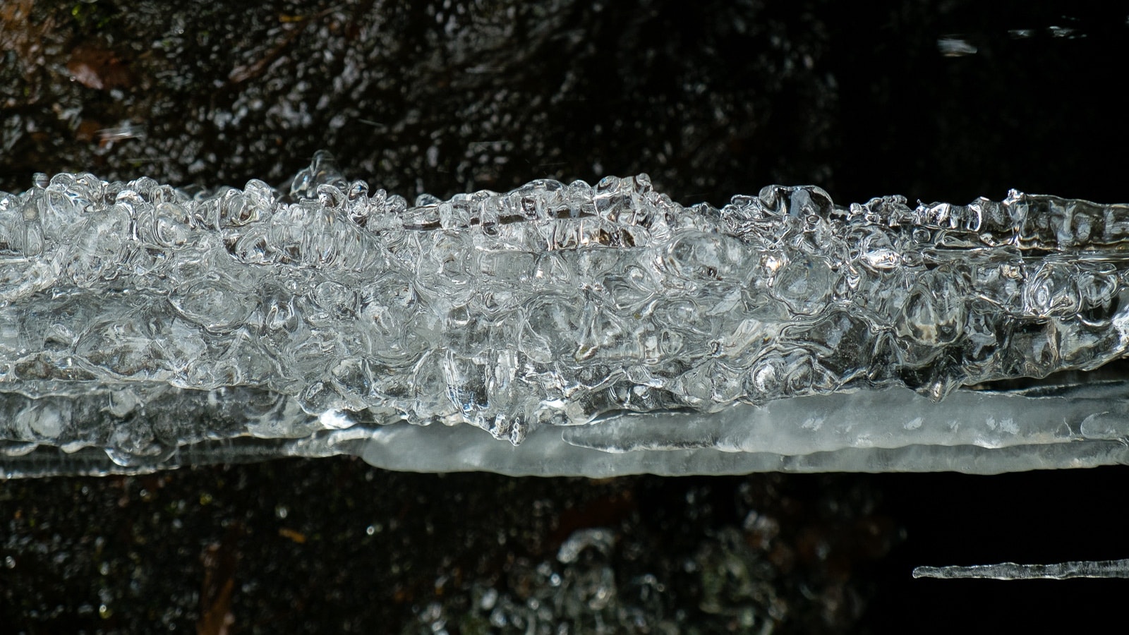 Gocce di ghiaccio sulla cresta di una cascata d'acqua. Una foto chiara che mostra ghiaccicole cadenti dall'alto, creando un'immagine molto suggestiva della bellezza naturale.