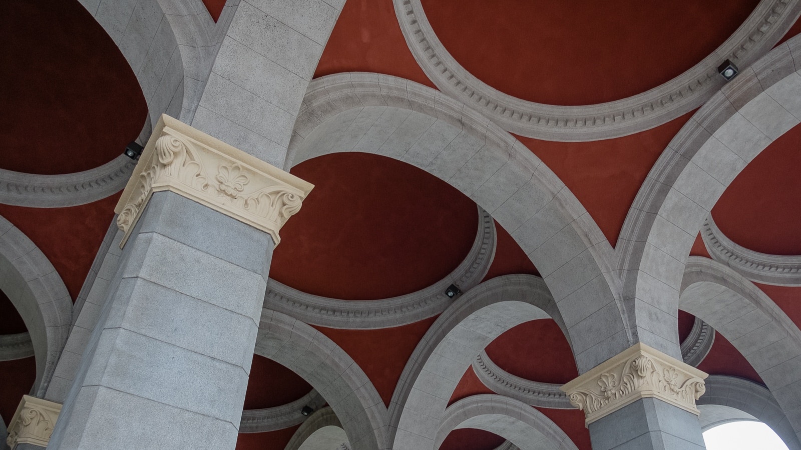 A series of elegant stone arches with intricate designs and columns beneath a rich red ceiling, showcasing architectural beauty and craftsmanship.