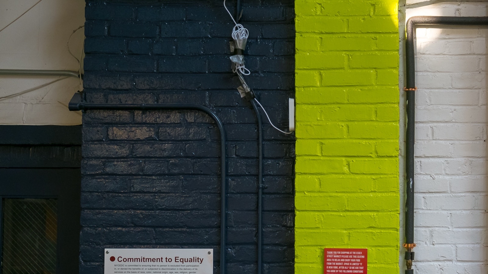 Parte della parete con due tonalità diverse, una sezione del muro di mattoni e un cartello vuoto sulla parte gialla.